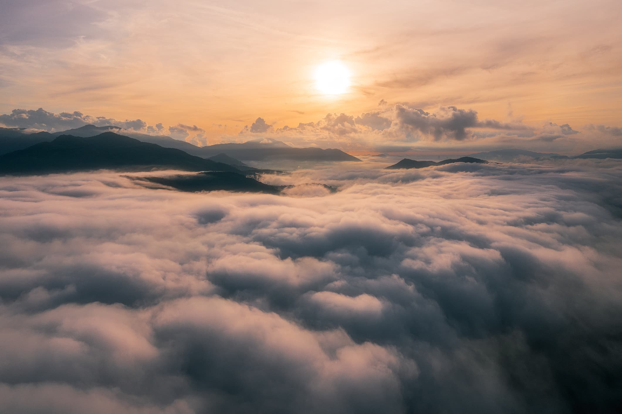 Mountains are bathed in a clouds, with just a few peaks poking out while the sun rises above them