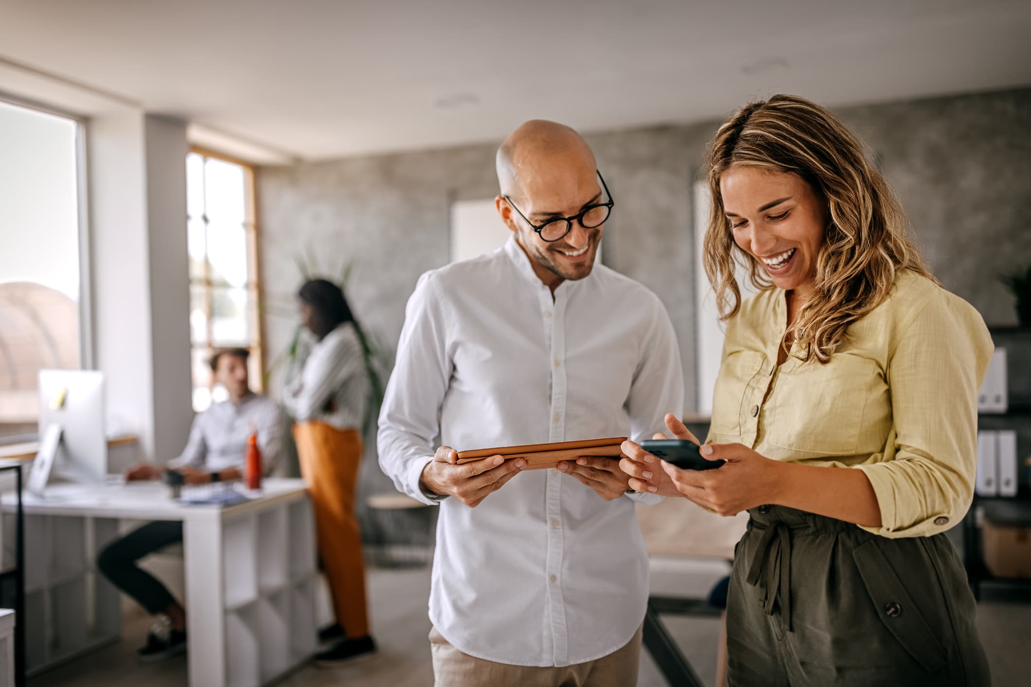 Businessman and businesswoman smiling looking at the screens of their electronic devices