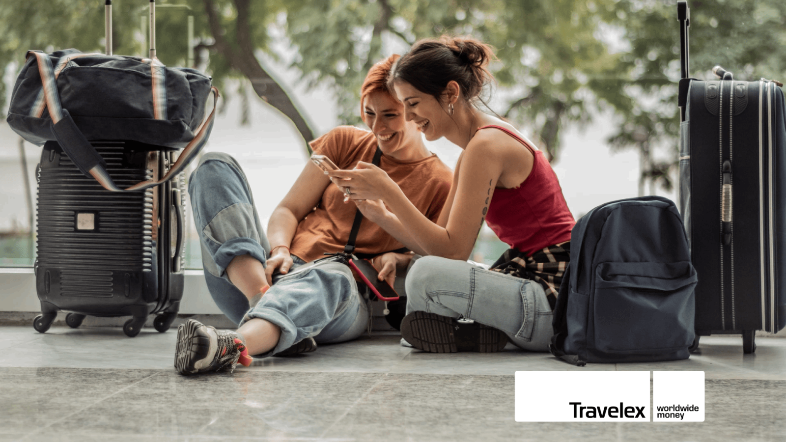 Two women sat on the floor in between two suitcases