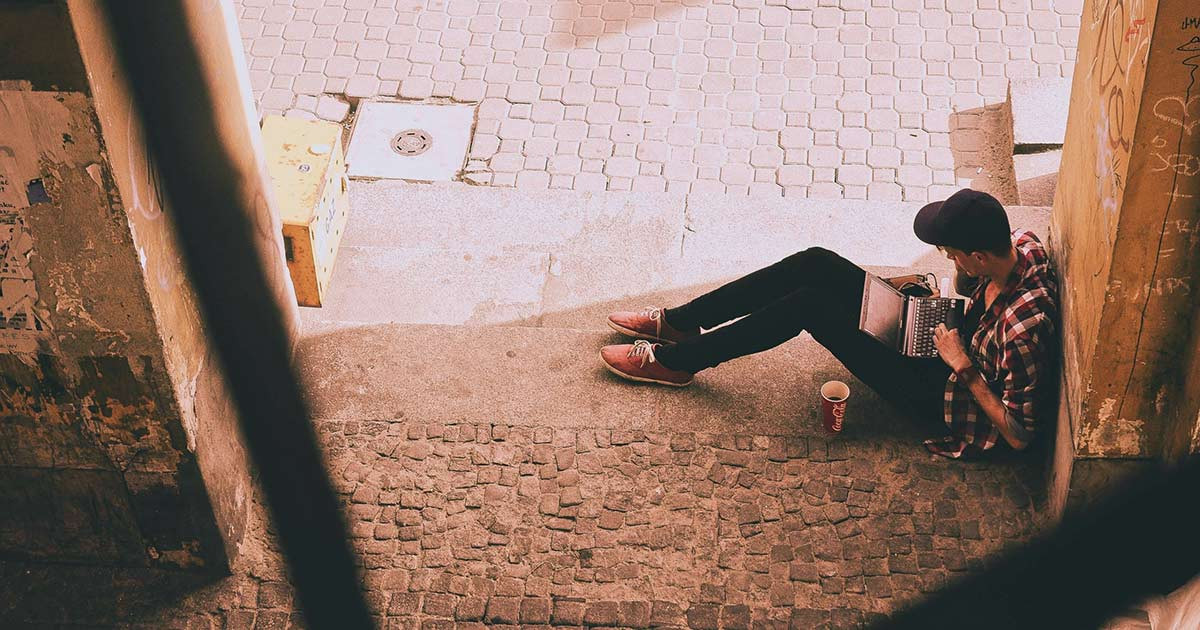 a remote worker working on his laptop outside in a doorway by a street