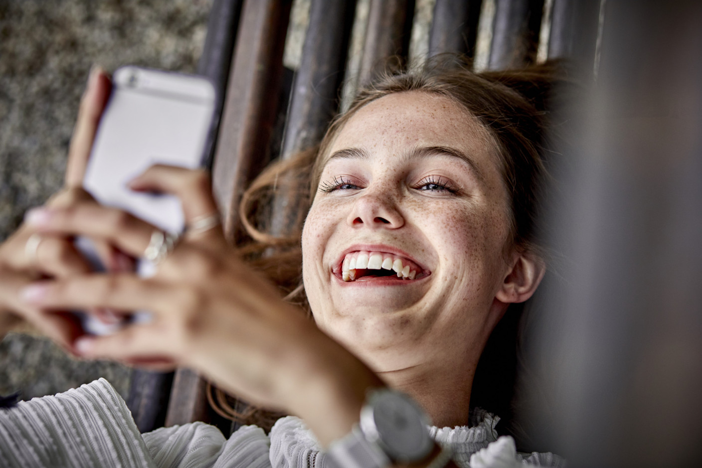 Customer Story - A happy woman lying down and holding her smartphone over her head.