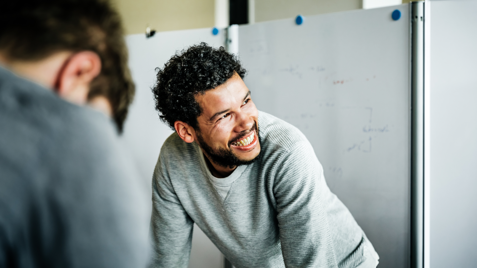 A smiling, beared man looks up to his right as he leans down.