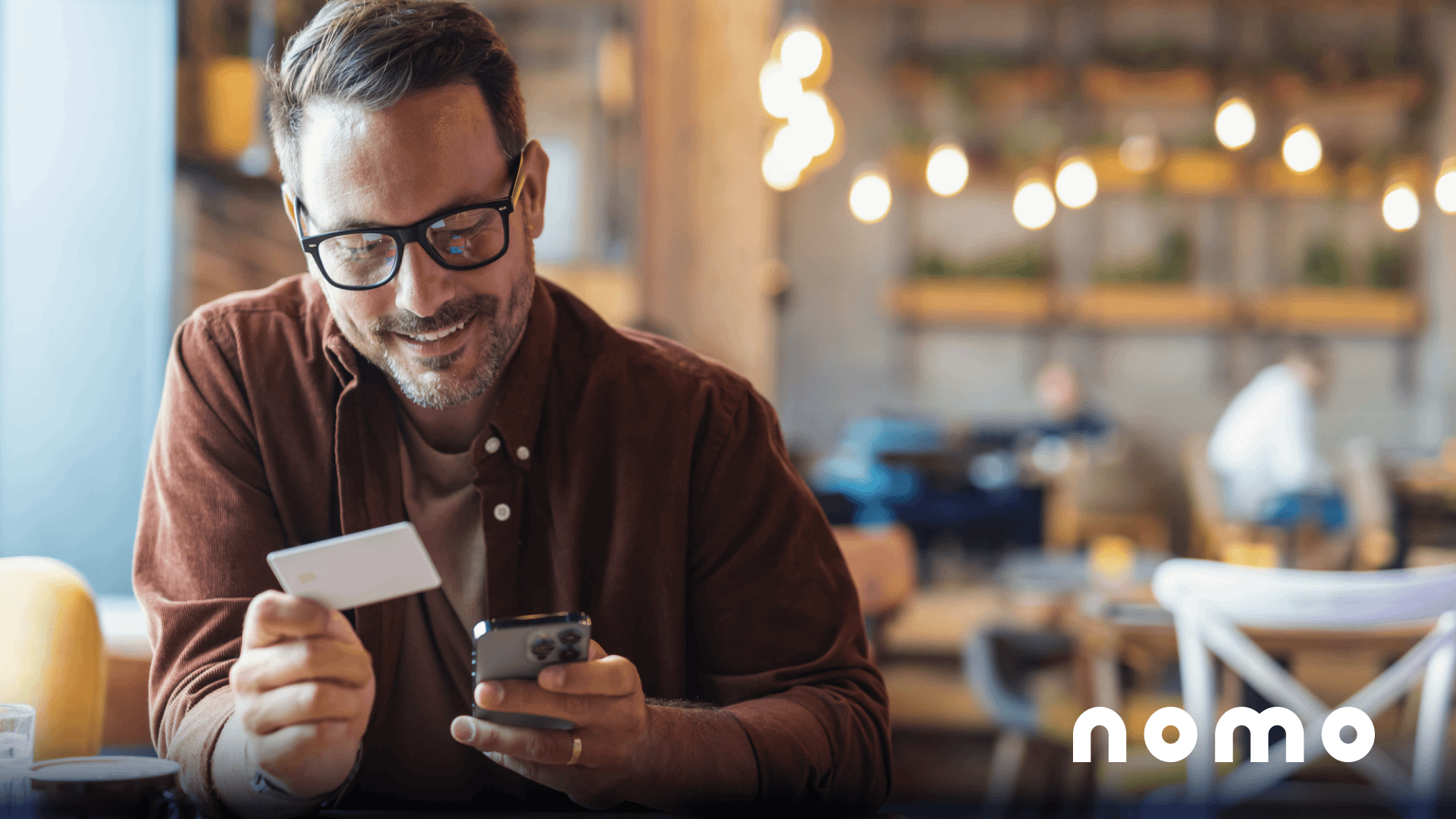 Nomo - A bespectacled man holds a bank card and his mobile phone